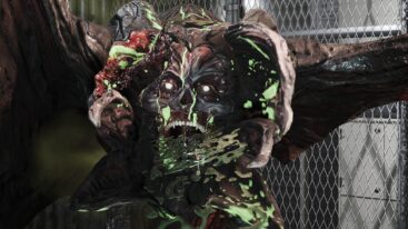 A mutated human with an open shell over its head, spewing acid at the camera