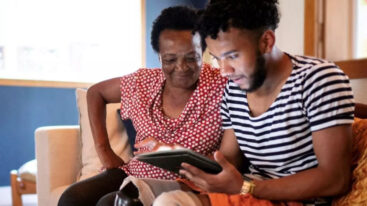 A son and his mother look at a tablet, with the son teaching